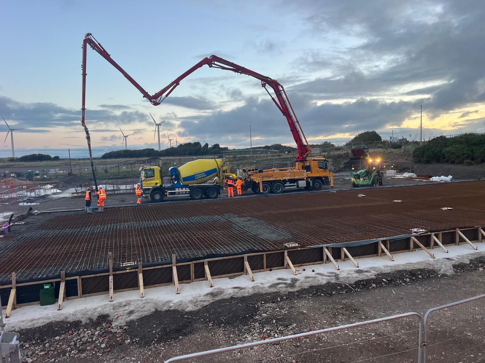 Boom pump placing concrete over a reinforced slab at dusk